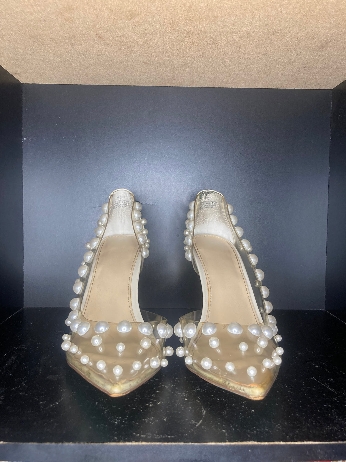 A pair of clear pointed-toe high heels decorated with white faux pearls