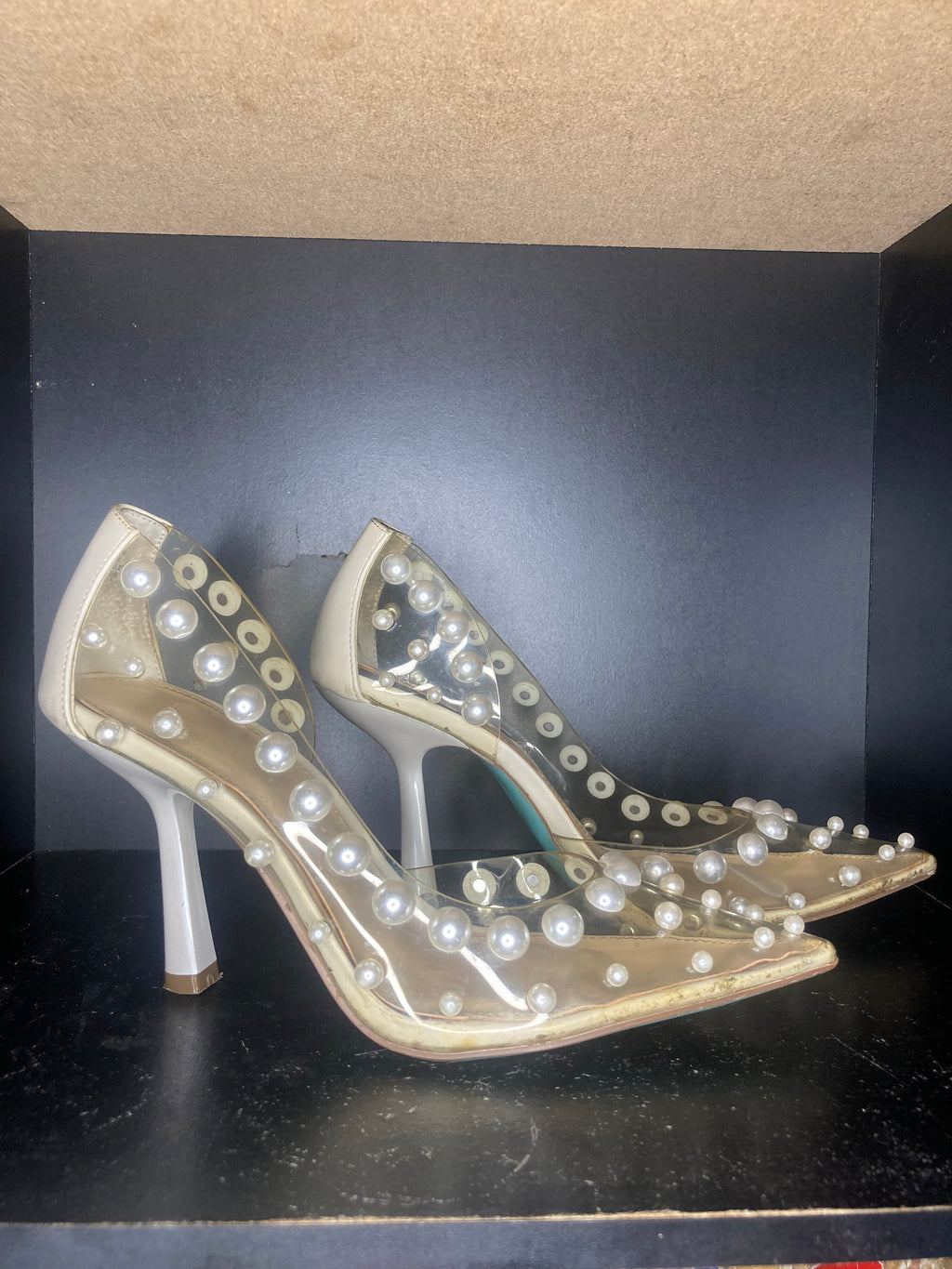 A pair of clear pointed-toe high heels decorated with white faux pearls