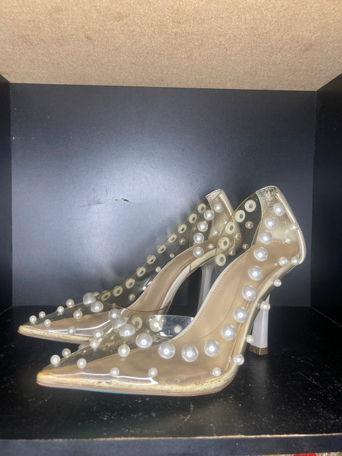 A pair of clear pointed-toe high heels decorated with white faux pearls.